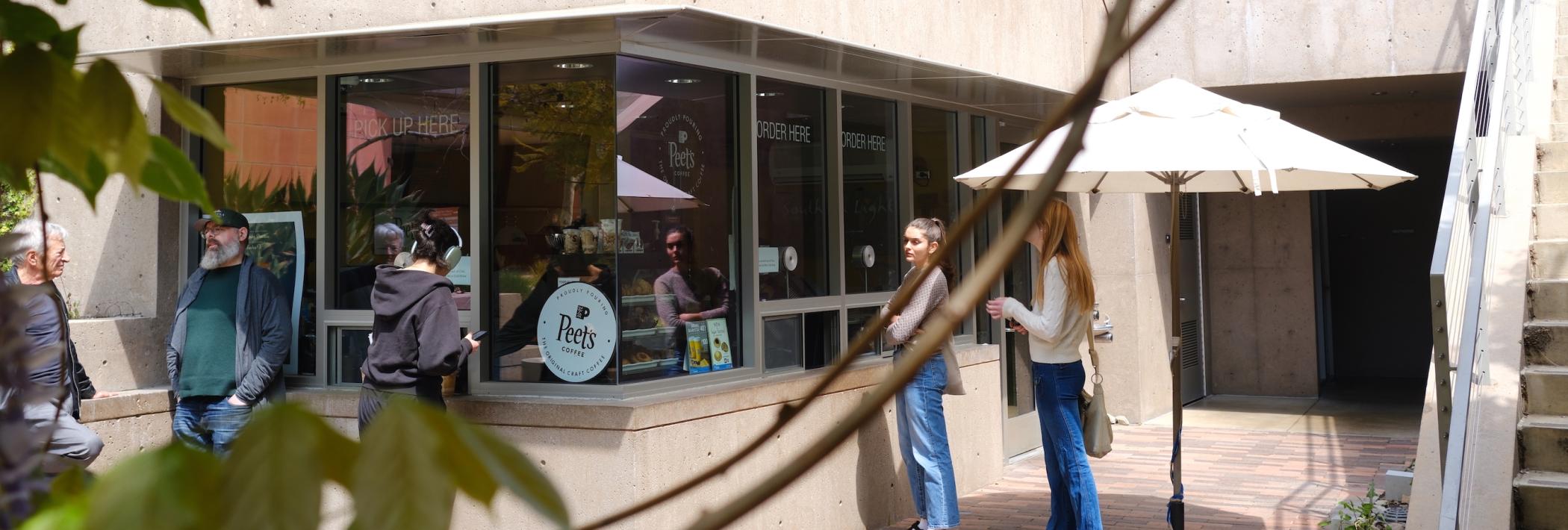 People stand outside a coffee shop with a sign saying Peet's in the window.
